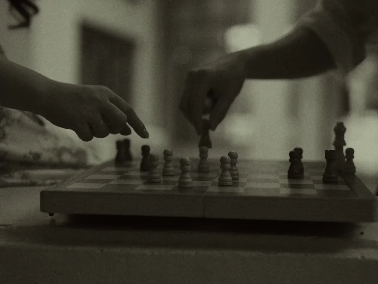 A hand moving a piece across a chessboard, in black and white