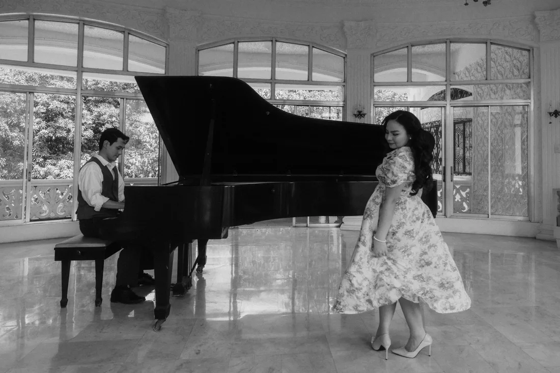 James at the grand piano while Elaine listens, in black and white