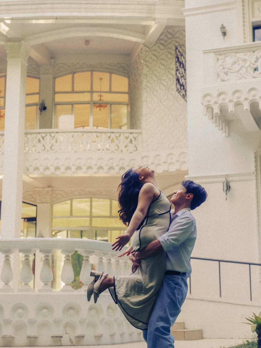 James lifting Elaine into the air by the white balustrade, both laughing